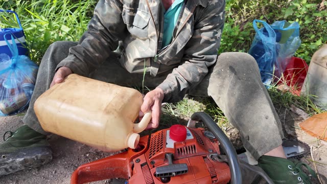 Farmer Refueling Chainsaw On Ground
